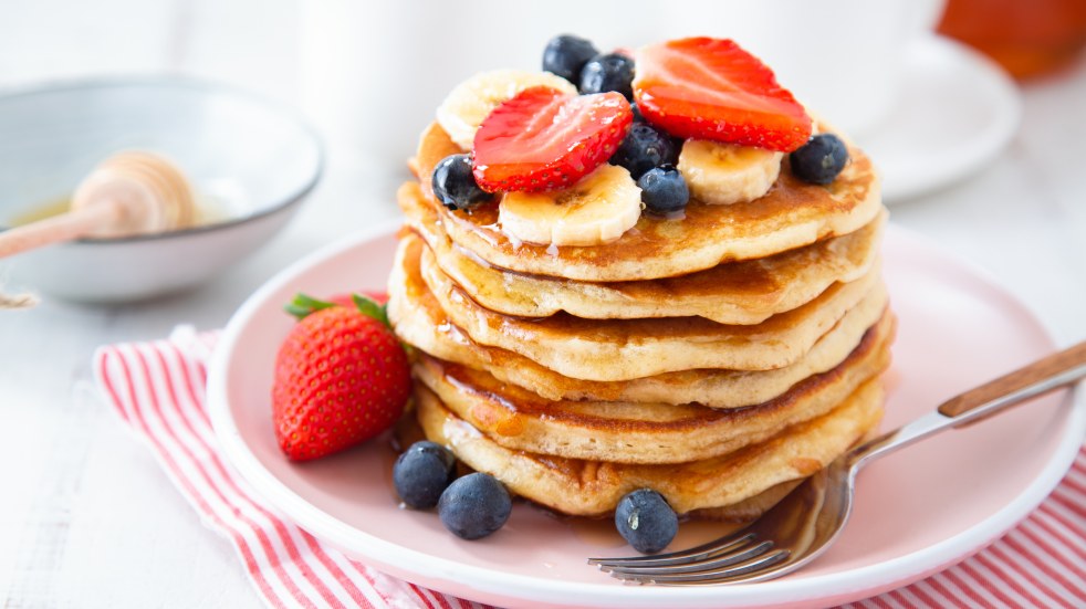 plate of pancakes topped with banana, blueberries and strawberries